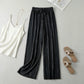 Luvia black wide-leg pleated plissé trousers styled in a flat-lay with a white camisole and beige slide sandals.