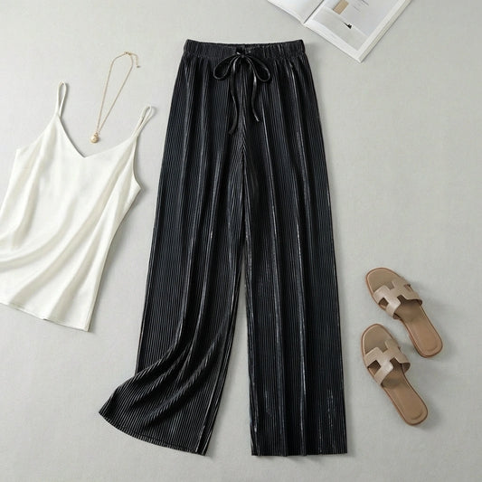 Luvia black wide-leg pleated plissé trousers styled in a flat-lay with a white camisole and beige slide sandals.