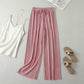 Luvia wide leg pleated plissé trousers in soft rose pink, styled in a flat-lay with a white camisole and beige sandals.