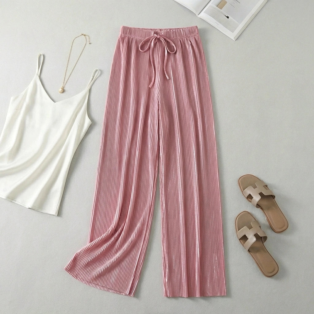 Luvia wide leg pleated plissé trousers in soft rose pink, styled in a flat-lay with a white camisole and beige sandals.