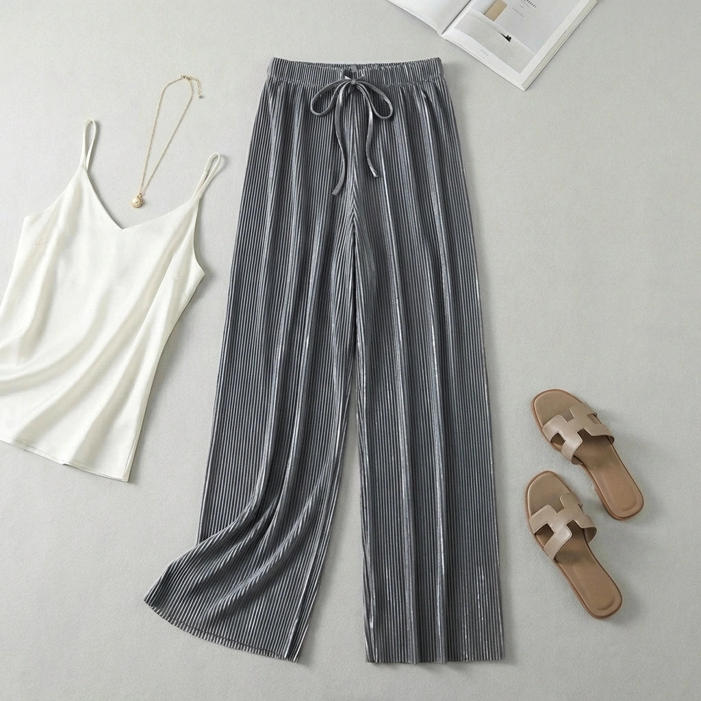Luvia wide-leg pleated plissé trousers in slate silver, styled in a flat-lay outfit with a white camisole and sandals.