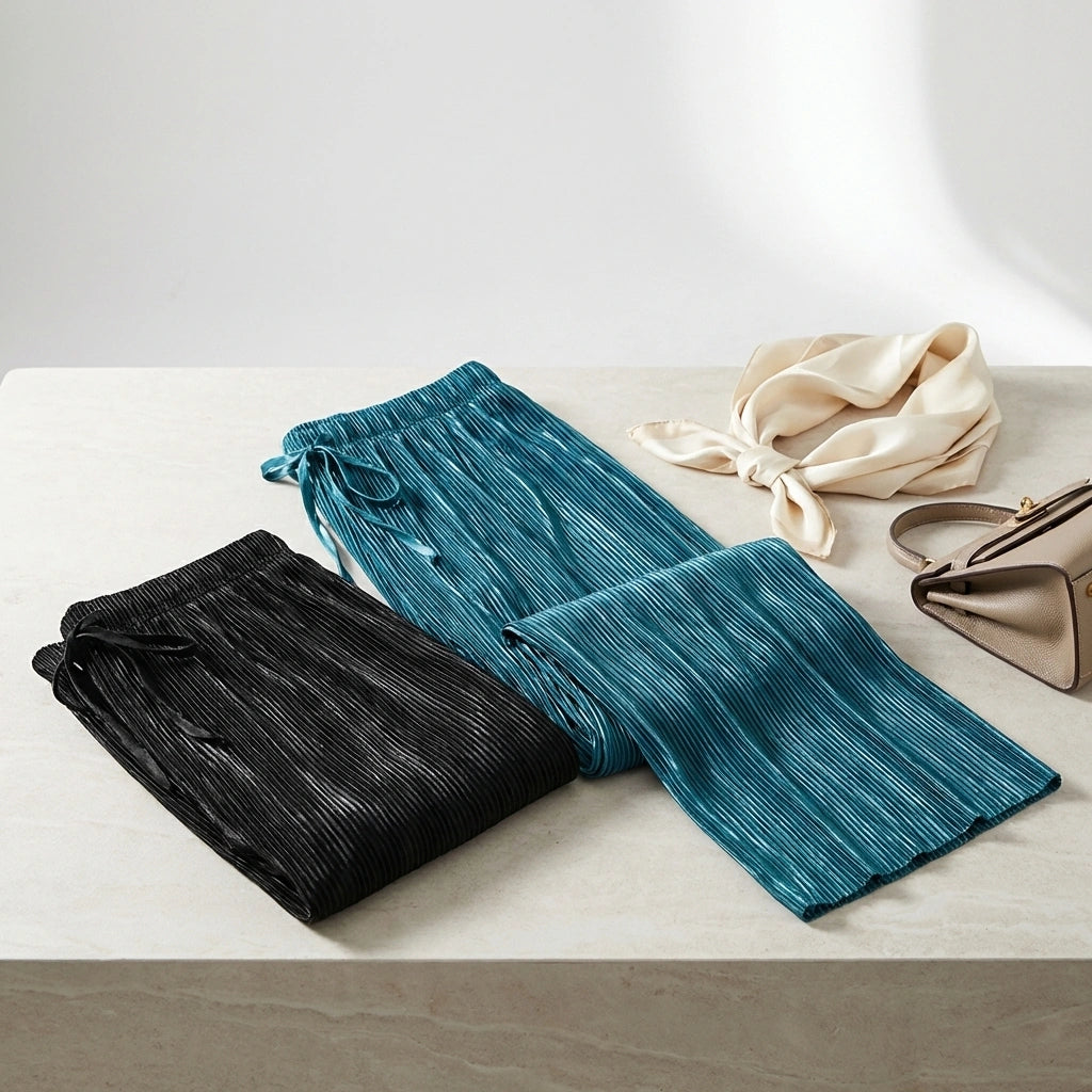 Luvia wide leg pleated plissé trousers in teal and black, displayed in a flat-lay arrangement with a silk scarf and handbag.