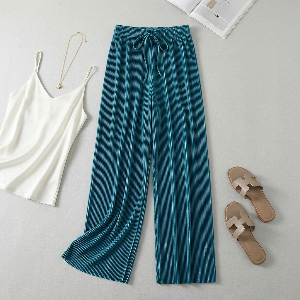 Luvia wide-leg pleated plissé trousers in deep teal, styled as a flat-lay outfit with a white camisole and beige sandals.