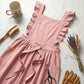 Luvina ruffled cotton pinafore apron in dusty rose, displayed in a flat-lay with dried flowers, scissors, and a ceramic mug.