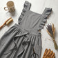 Luvina ruffled cotton pinafore apron in slate gray, displayed in a flat-lay with gardening tools, dried flowers, and a ceramic mug.