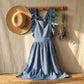 Luvina ruffled cotton pinafore apron in slate gray hanging on a wooden rack with a straw hat and dried lavender, cottagecore aesthetic.