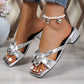 Elegant silver heeled mules featuring a prominent fabric rose embellishment on the strap, displayed on a model's feet with a square open-toe design and chunky block heel.