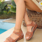 A woman's feet wearing brown Lyraia comfort wedge sandals with peep-toe design, adjustable hook-and-loop straps, and white contrast stitching, set in a relaxed outdoor lifestyle scene by a pool.