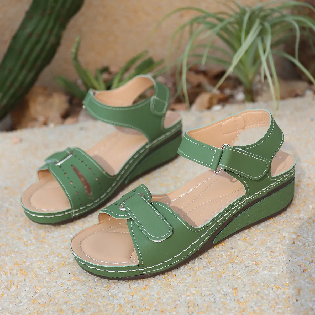 Green Lyraia comfort wedge sandals with peep-toe front and adjustable hook-and-loop straps shown in a natural outdoor setting with sand and plants.