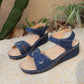 Navy blue Lyraia comfort wedge sandals with peep-toe design and contrasting white stitching, shown from a three-quarter angle on a sandy, outdoor-inspired background.
