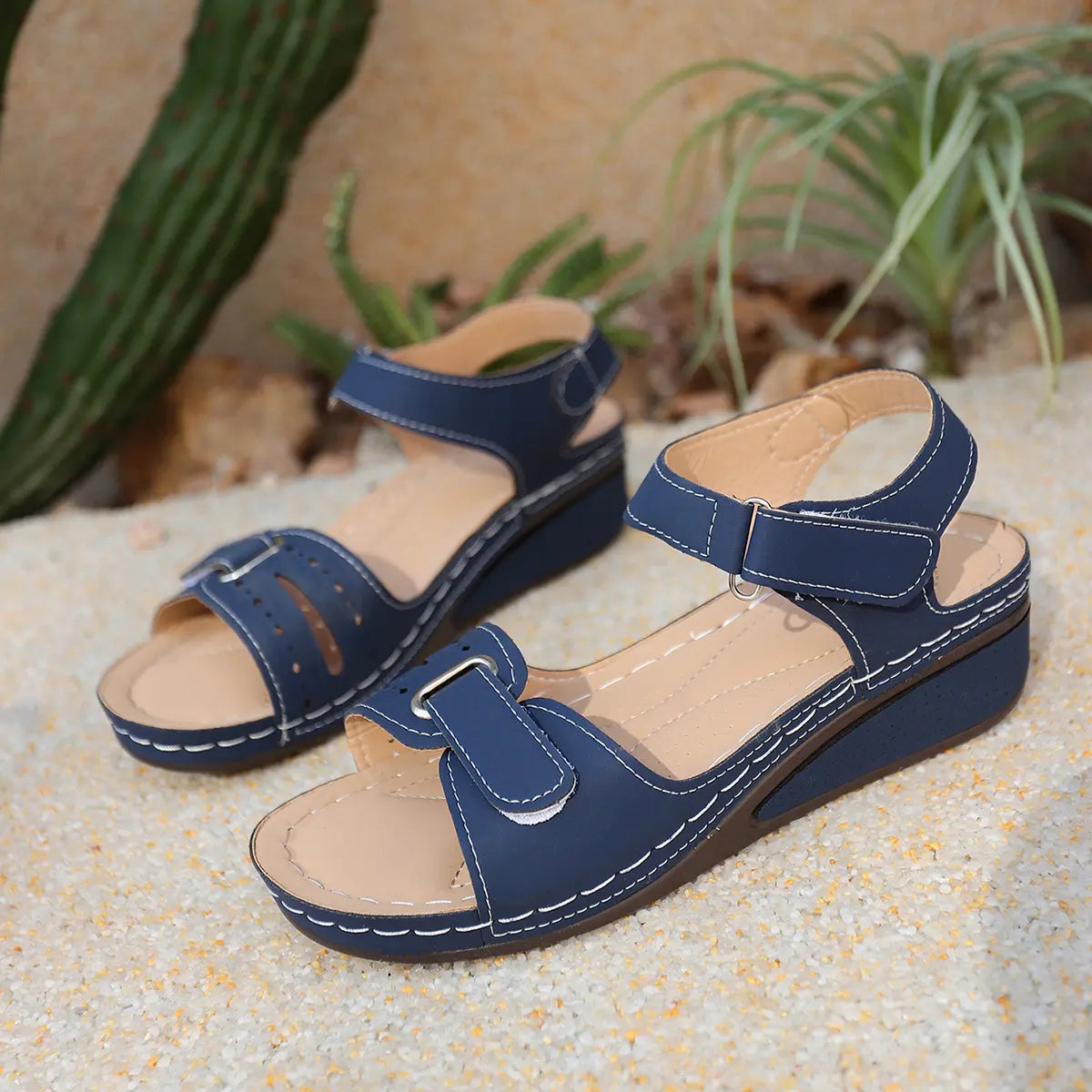 Navy blue Lyraia comfort wedge sandals with peep-toe design and contrasting white stitching, shown from a three-quarter angle on a sandy, outdoor-inspired background.