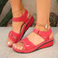 Red Lyraia comfort wedge sandals on a woman's feet, featuring a peep-toe design, adjustable hook-and-loop straps, and contrast white stitching, shown in a lifestyle outdoor setting.