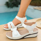White Lyraia comfort wedge sandals shown on a model's foot with a second sandal beside it, featuring peep-toe design, adjustable straps, and contrast stitching in a lifestyle setting by a pool.