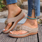 Lyraka women's beige thong sandals with a delicate fabric flower embellishment and gold studs, shown worn with jeans and a turquoise anklet on a wooden deck.