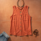 Makori women's coral textured sleeveless V-neck tank top with prominent faux-wood buttons and a chest pocket, artfully flat-laid with layered bohemian beaded necklaces and blue denim on a warm terracotta background.