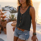Makori Midnight Black sleeveless V-neck tank top with textured fabric and faux-wood buttons, styled on a model with denim shorts in a bohemian outdoor setting.