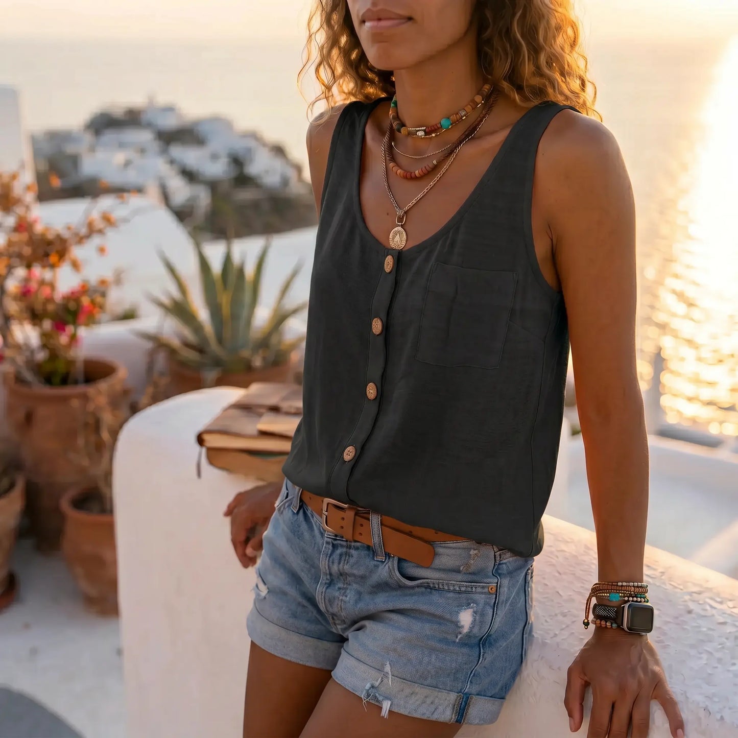 Makori Midnight Black sleeveless V-neck tank top with textured fabric and faux-wood buttons, styled on a model with denim shorts in a bohemian outdoor setting.