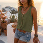 Women's Makori olive green sleeveless V-neck textured tank with faux-wood buttons and a chest pocket, worn by a woman outdoors with denim shorts and layered necklaces.
