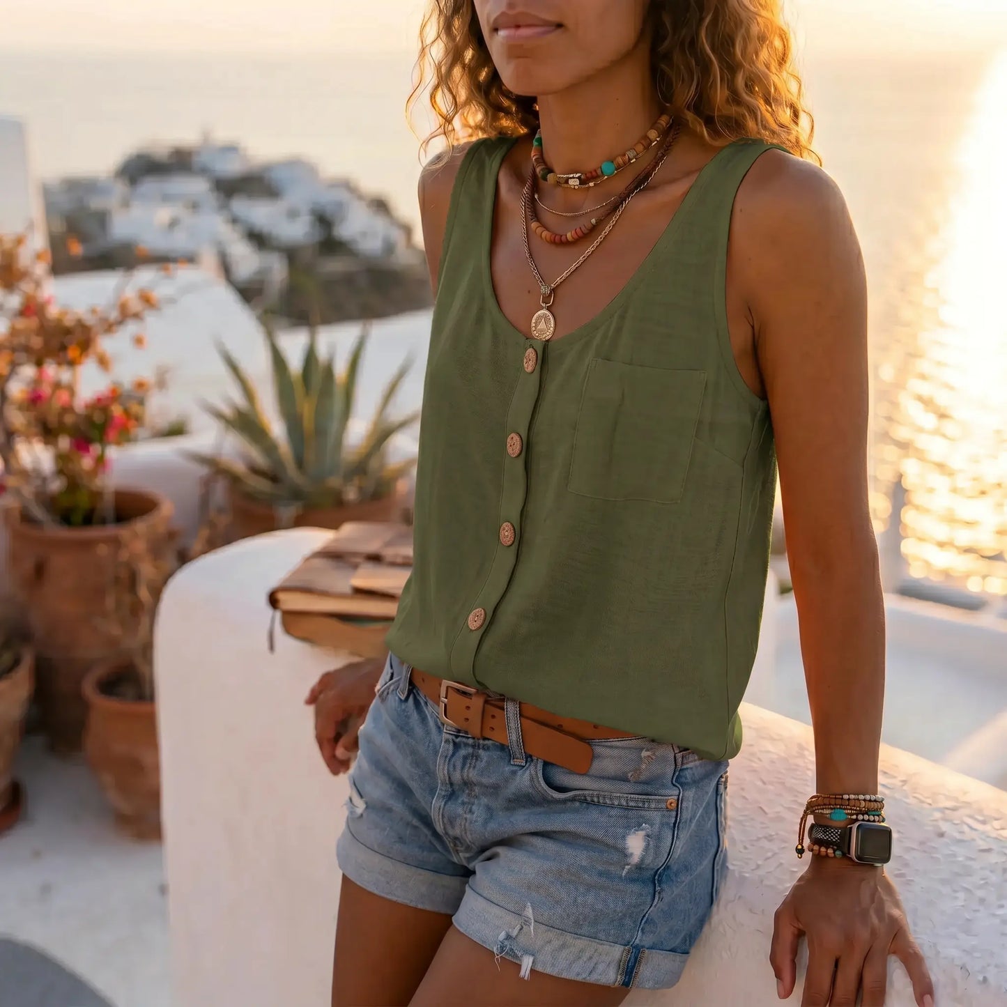 Women's Makori olive green sleeveless V-neck textured tank with faux-wood buttons and a chest pocket, worn by a woman outdoors with denim shorts and layered necklaces.