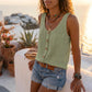 Makori sage green sleeveless V-neck tank, with textured fabric and faux-wood buttons, worn by a model in an elegant outdoor setting.