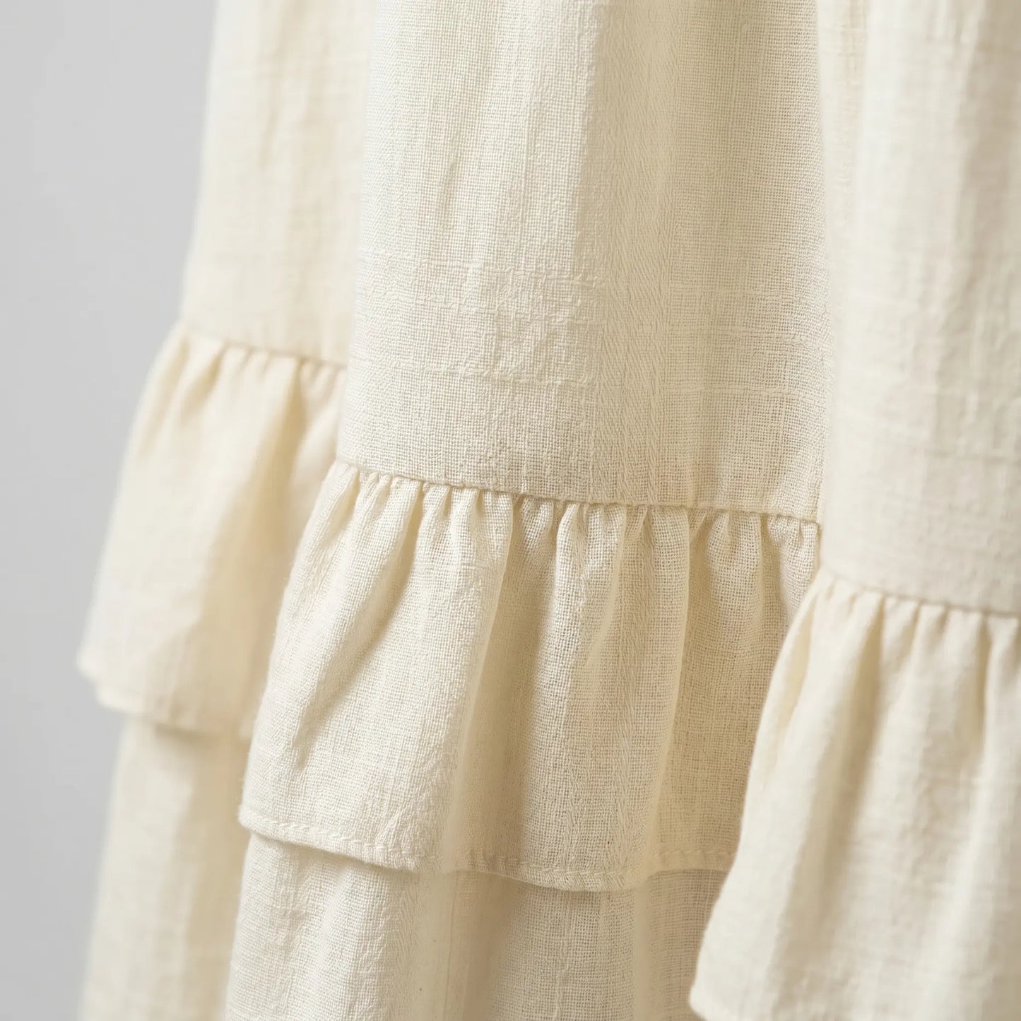 Close-up of the Zyrak vanilla cream maxi dress, highlighting the subtle micro-crinkle textured fabric and delicate ruffled tier detail. Elegant design.