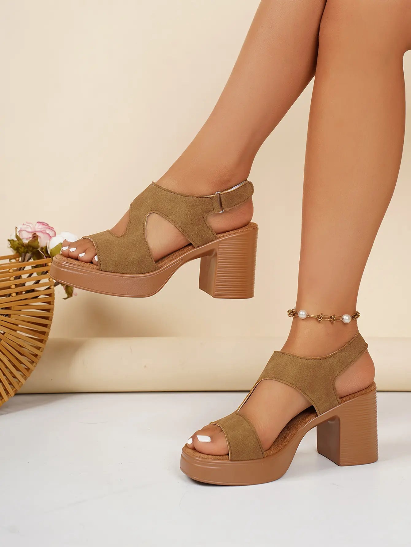 Model's legs wearing warm tan suede-finish platform sandals with a V-cut forefoot strap and a thick, ribbed block heel, styled with a pearl anklet on a soft, neutral background.