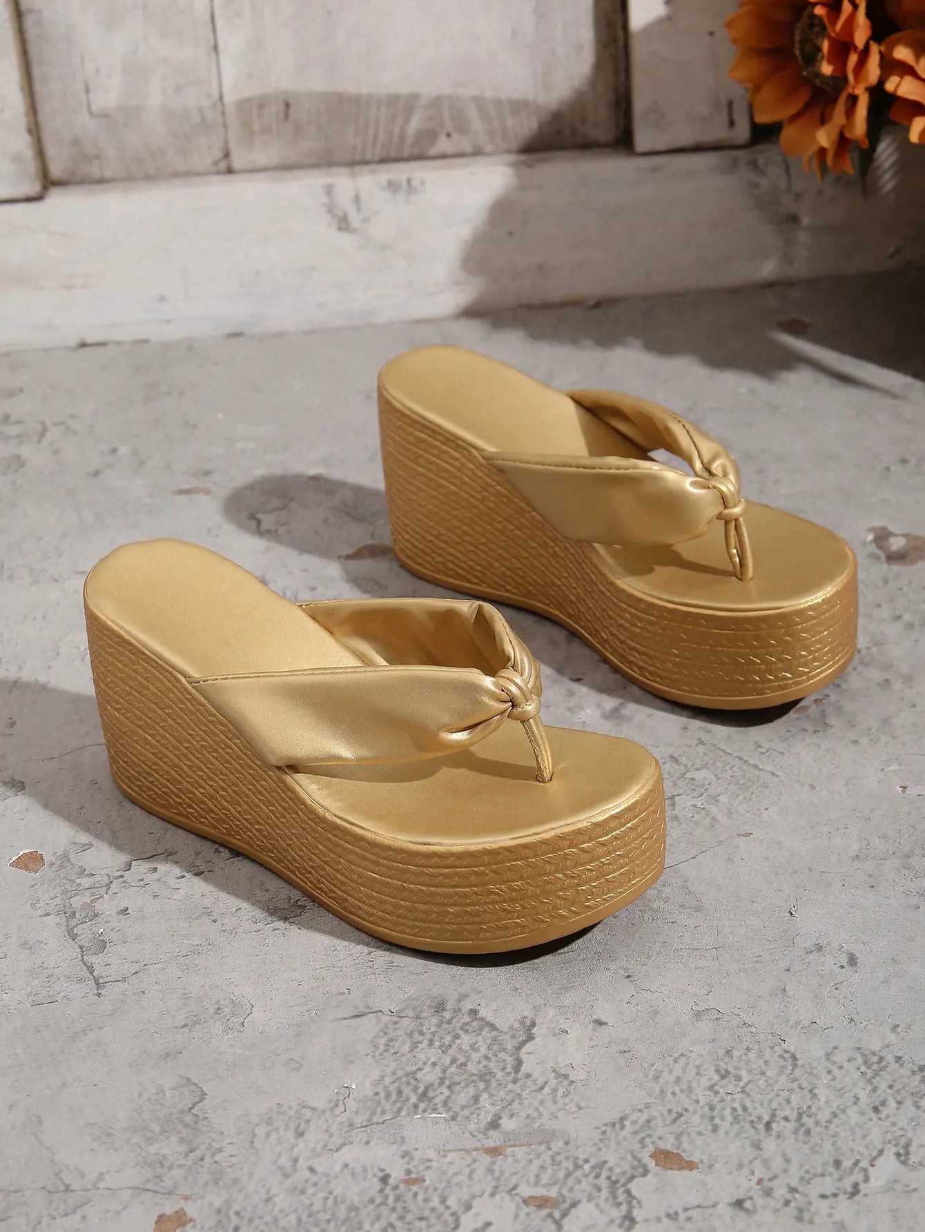 Metallic gold wedge platform flip-flops with a knotted toe strap and a textured woven-effect platform base, shown from a three-quarter angle.