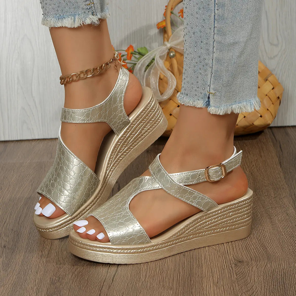 Golden metallic peep-toe wedge sandals with embossed crocodile texture and T-strap, styled with distressed denim jeans on a model's feet.