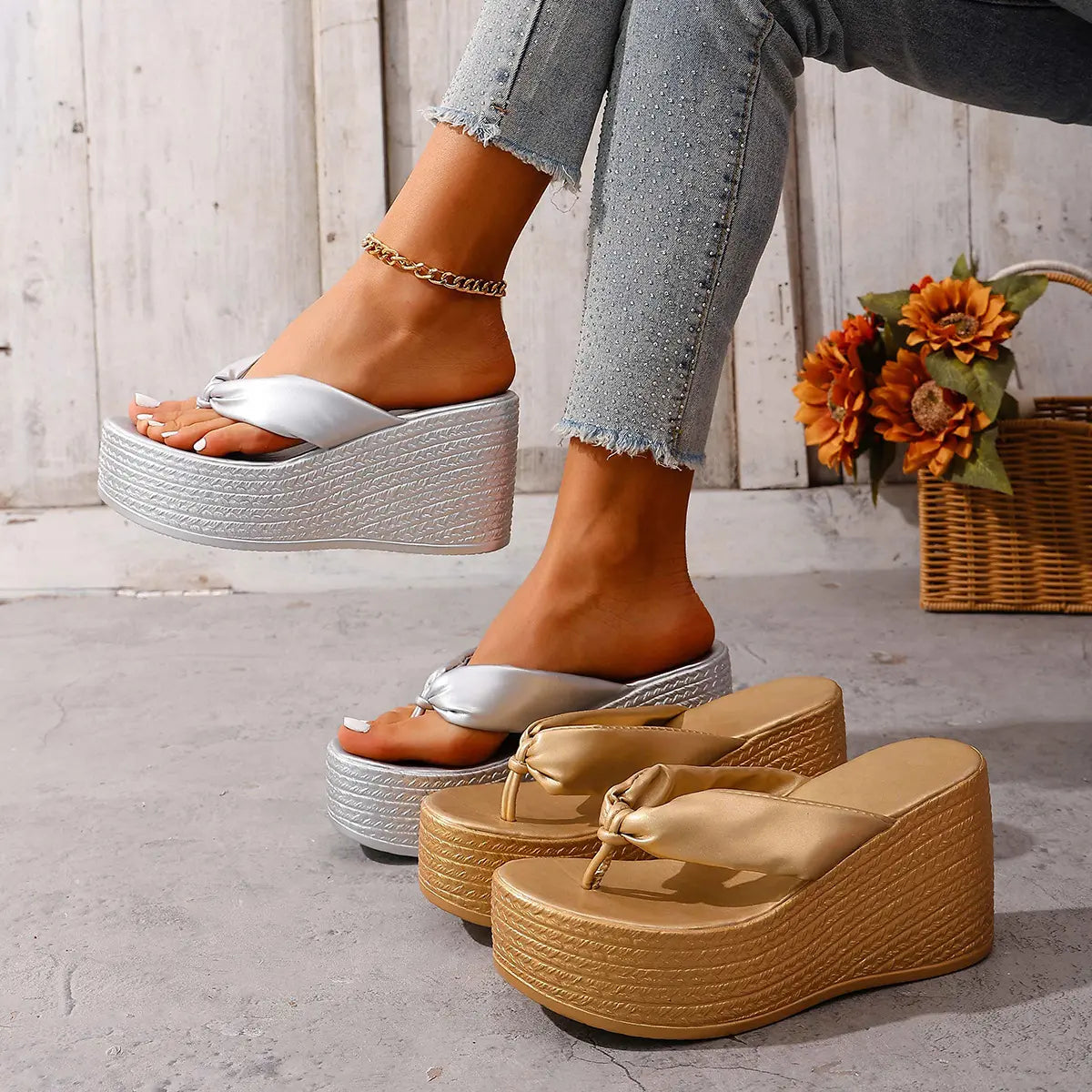 Stylish metallic wedge platform flip-flops in shimmering silver and champagne gold, worn on a woman's feet with ripped jeans and an anklet, showcasing the knotted toe strap and textured platform base.