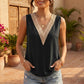 A woman wears a sleeveless black V-neck blouse with intricate beige crochet trim, styled with denim shorts in an outdoor, bohemian-inspired setting.