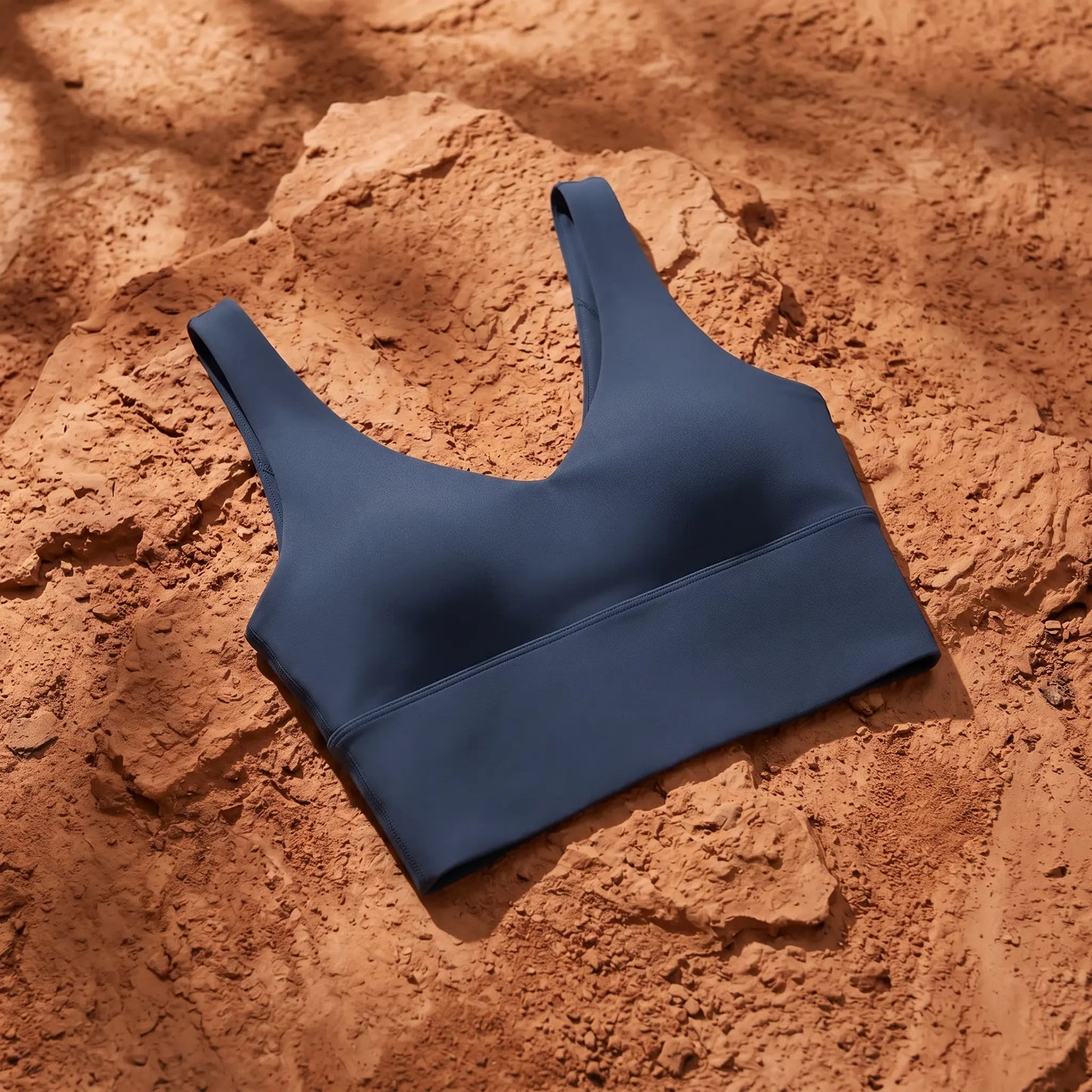 Zykari Midnight Black yoga sports bra with scoop neck and wide straps. Smooth, matte fabric laid flat on a rich terracotta textured background.