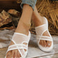 A pair of white mesh wedge slide sandals worn by a woman with an anklet, styled with distressed denim jeans on a rustic wooden surface with a straw background.