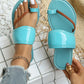 Ocean blue patent toe-thong flat sandals on a model's foot, showcasing the glossy patent strap, braided toe loop, and contrasting white stitching on the flat sole. Accented with a gold chain anklet.