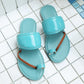 Turquoise patent leather toe-thong slide sandals with braided brown straps, shown on a white tiled background. Features a glossy wide strap and a flat sole with white contrast stitching.