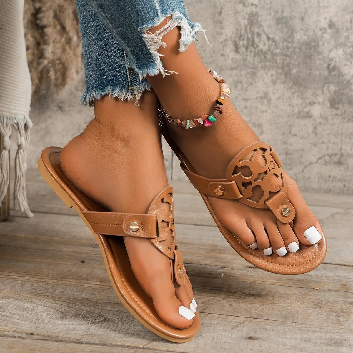 A pair of tan Miraya embellished flat thong sandals shown on a woman's feet, featuring an ornate circular cut-out vamp with gold stud accents and a flat rubber sole.