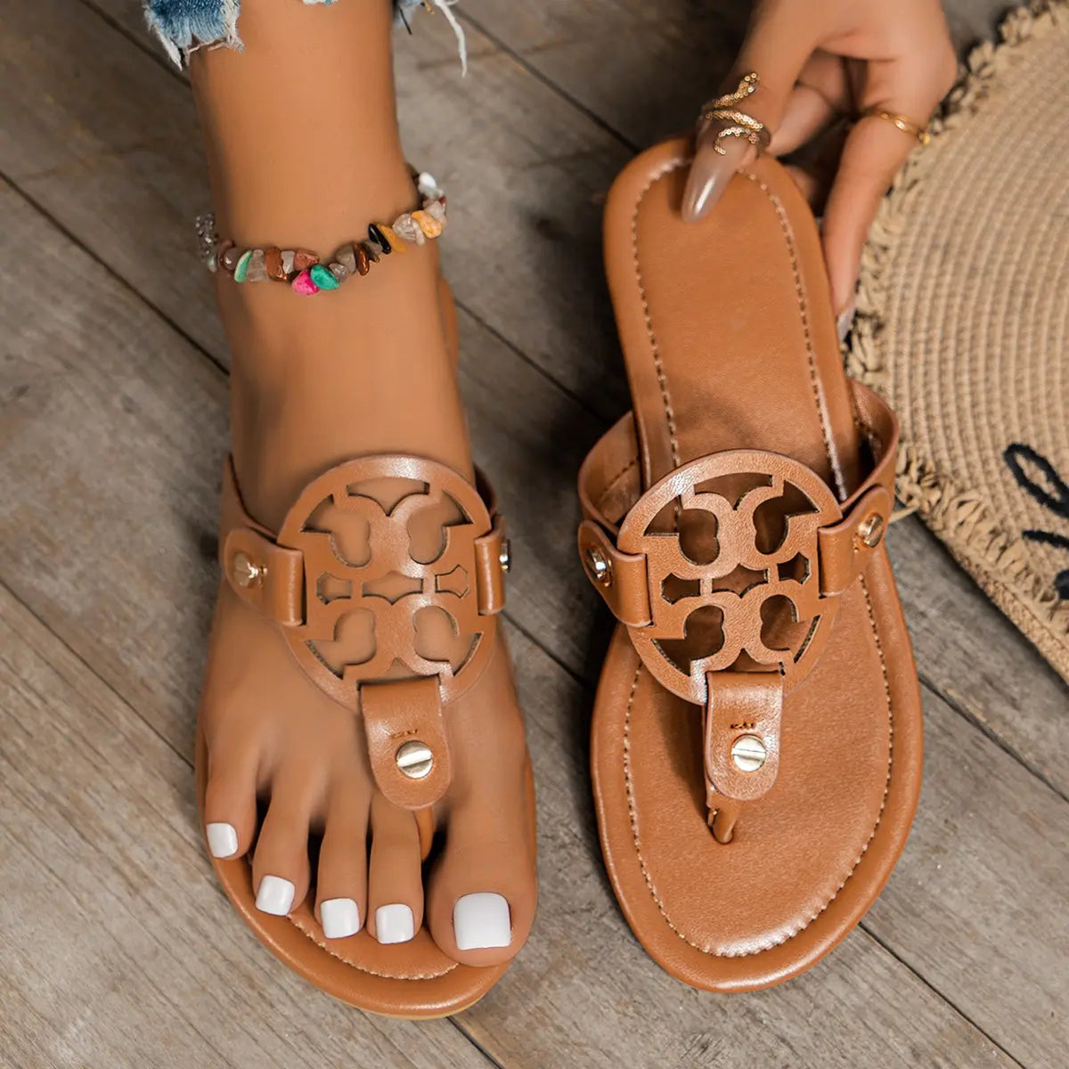 Miraya tan embellished flat thong sandals with ornate circular cut-out vamp and gold stud accents, worn on feet with white pedicure and colorful beaded anklet.