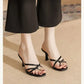 Elegant black strappy heeled mules with thin criss-cross straps, showcasing an open almond toe and slender stiletto heel worn by a model with black trousers.
