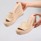 Hands presenting Miwazi khaki beige woven raffia espadrille wedge sandals with a 10.2cm braided jute heel and square open toe.