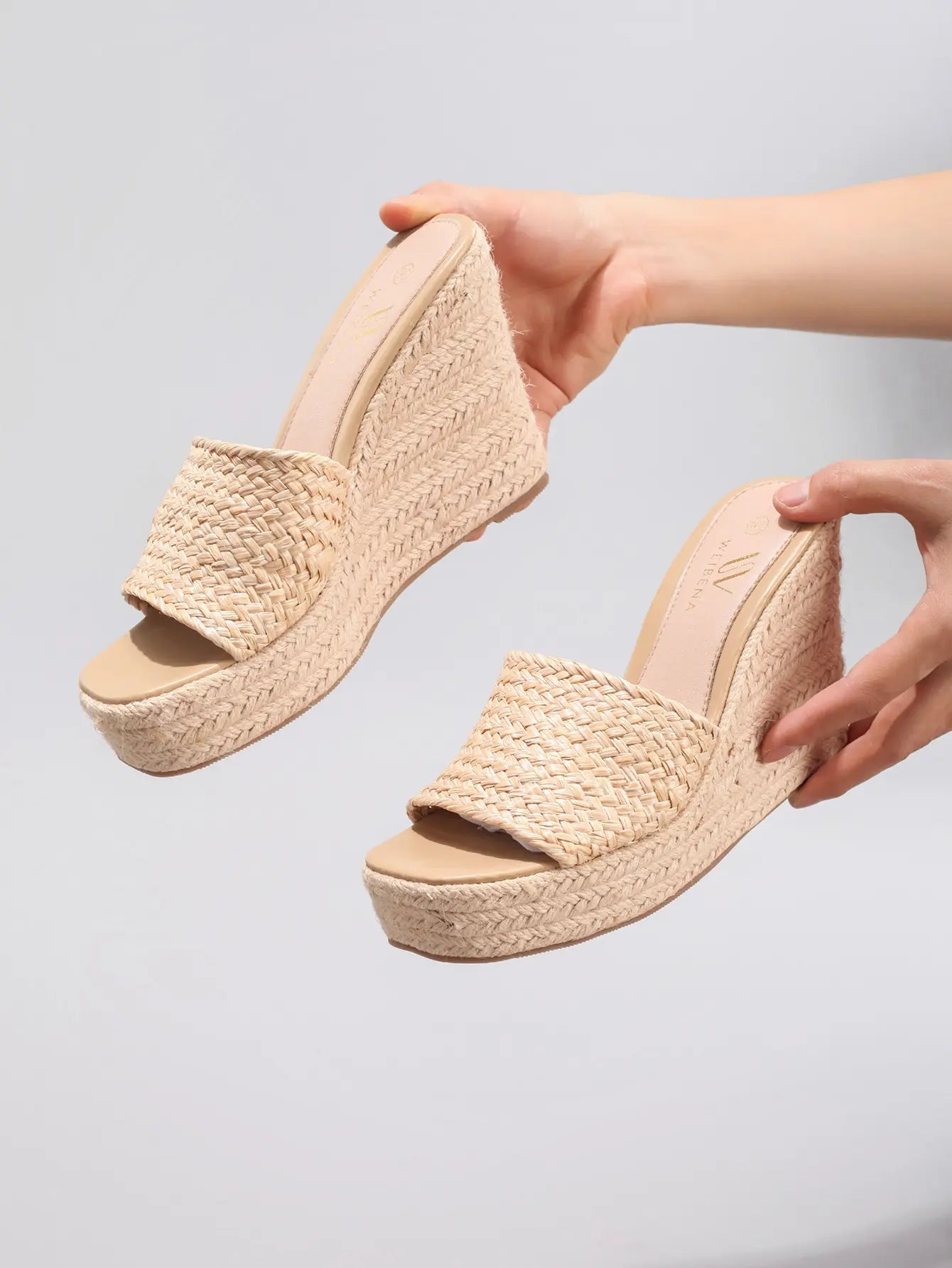 Hands presenting Miwazi khaki beige woven raffia espadrille wedge sandals with a 10.2cm braided jute heel and square open toe.