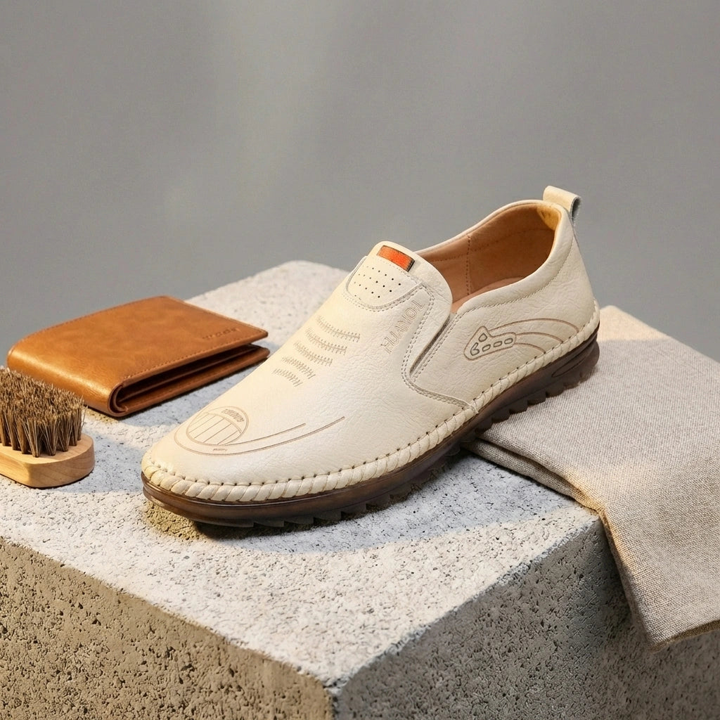Mokasso men's comfort driving loafer in ivory cream vegan leather, three-quarter view styled with wallet and brush to show hand-stitched details.