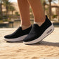 Myrkos Midnight Black slip-on knit sneakers, featuring a thick white platform sole with a visible heel air cushion, worn by a person standing on a textured outdoor path.