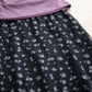 Close-up detail of the Myrven black maxi skirt, showcasing its delicate lavender and white micro-floral print on flowing fabric, with the dusty mauve off-shoulder top.