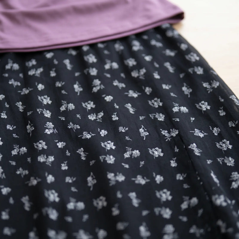 Close-up detail of the Myrven black maxi skirt, showcasing its delicate lavender and white micro-floral print on flowing fabric, with the dusty mauve off-shoulder top.