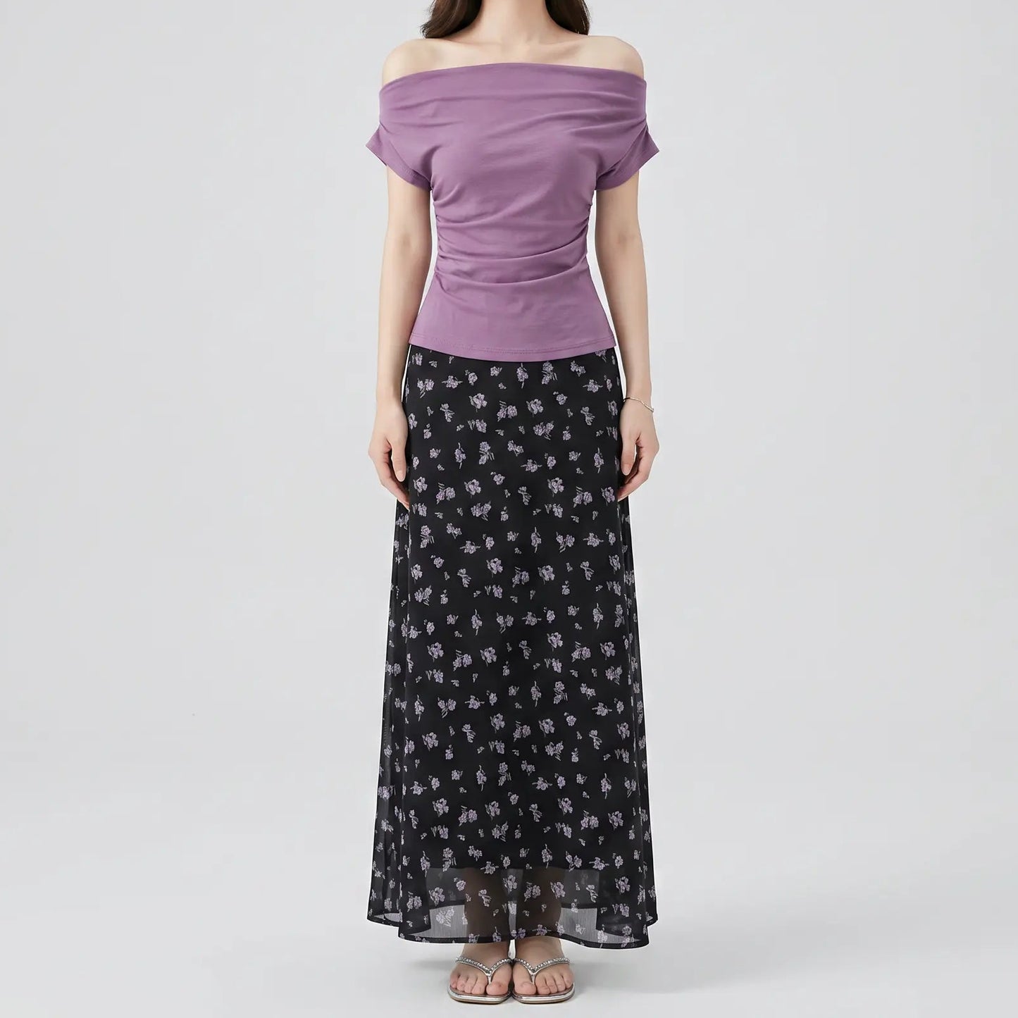 Model wearing Myrven's off-shoulder dusty mauve top with draped ruching and a black maxi skirt with delicate lavender floral print.
