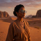 Woman in a desert landscape at sunset, wearing Nalani matte black metal square clip-on sunglasses with grey polarized lenses, looking towards the horizon.