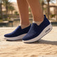 Exquisite navy blue knit slip-on sneakers, featuring a thick white platform sole with a visible heel air cushion, worn outdoors on a sandy path. The breathable upper provides effortless comfort.
