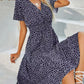 A model wears a navy ditsy floral V-neck midi dress with short flutter sleeves and a smocked cinched waist, styled with a necklace and bracelet.