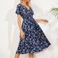 Women's navy blue midi dress with a ditsy floral print, featuring a V-neck, short flutter sleeves, and a cinched smocked waist, shown on a model in a relaxed pose.