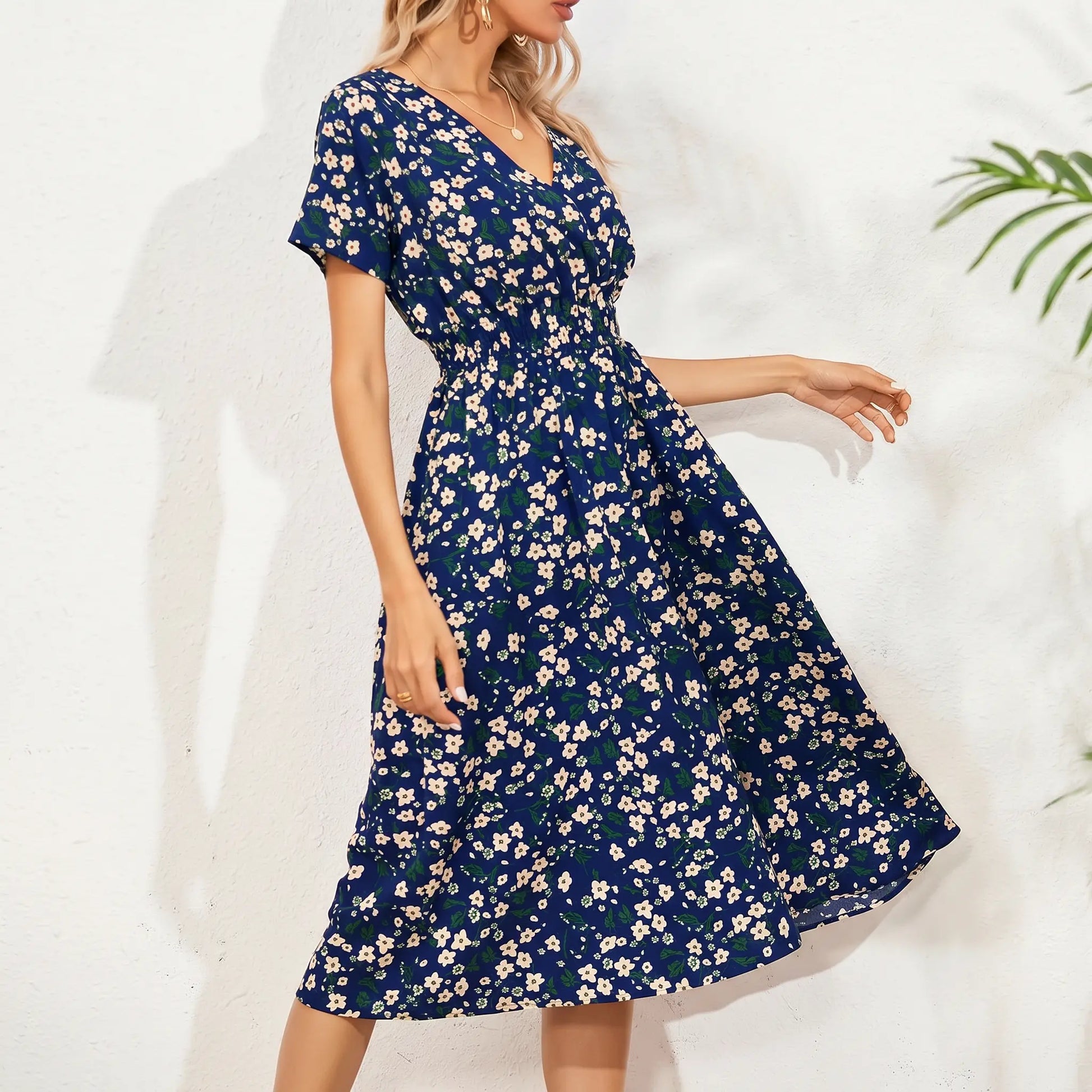 Women's navy blue midi dress with a ditsy floral print, featuring a V-neck, short flutter sleeves, and a cinched smocked waist, shown on a model in a relaxed pose.