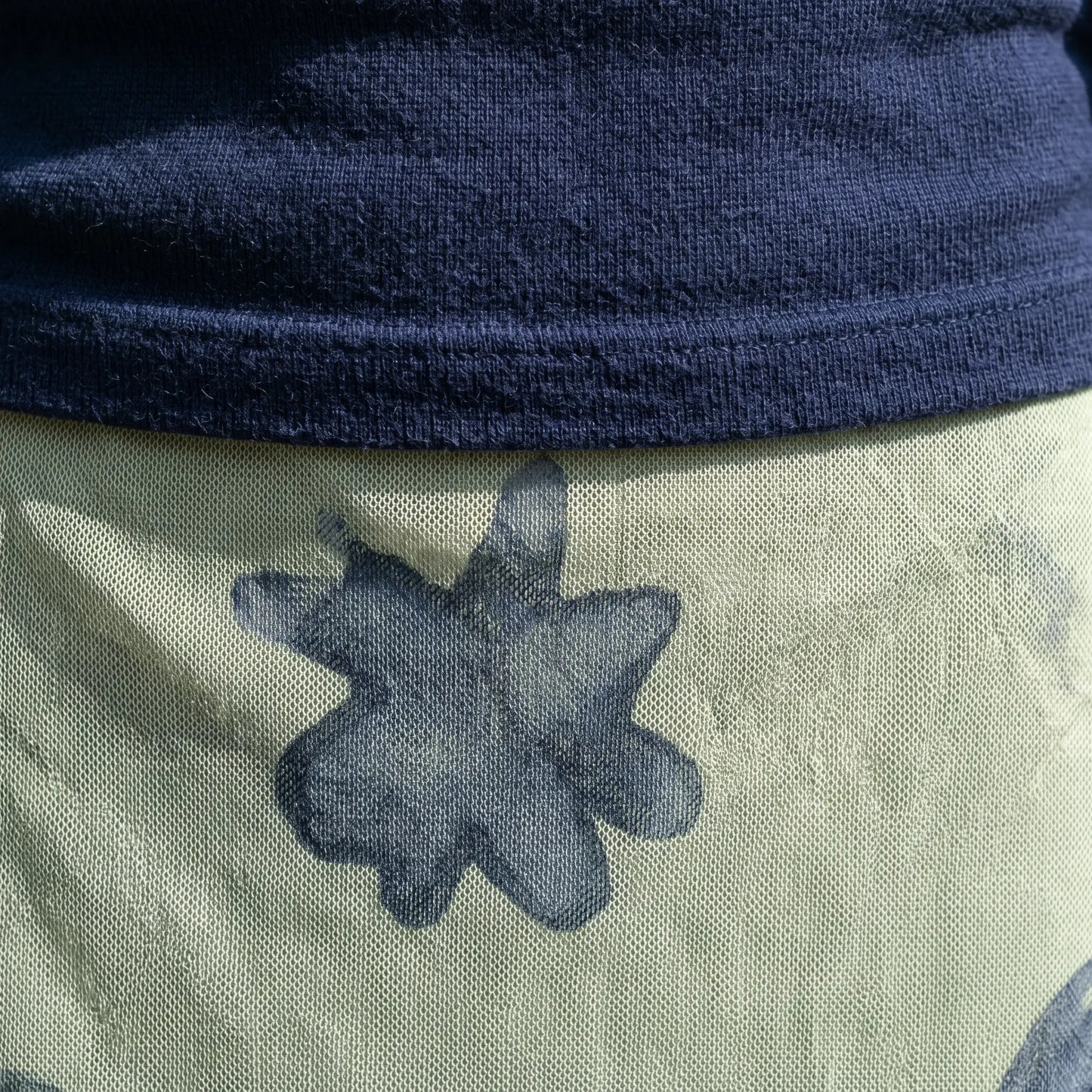 Close-up detail of the deep navy knit fabric from the V-neck top and the pale sage green mesh overlay of the maxi skirt with dark abstract patterns.